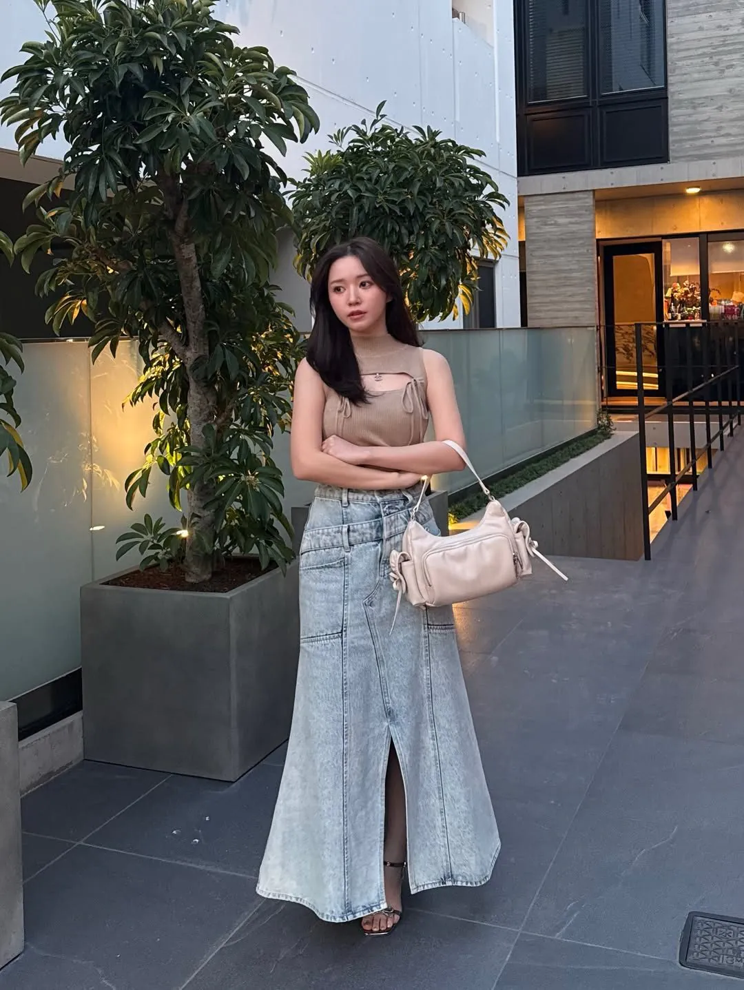 woman wearing tan sleeveless top and long denim skirt with a front slit.
