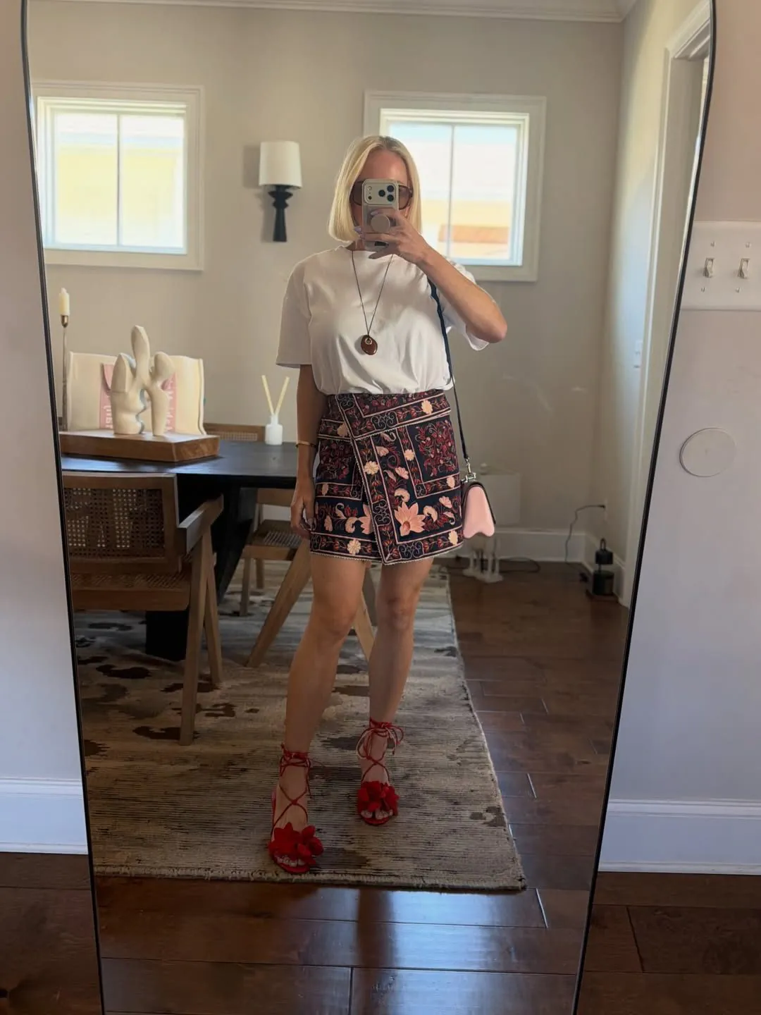 woman in white t-shirt and colorful floral mini wrap skirt with red lace-up sandals.