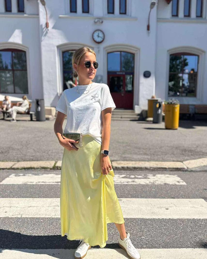 woman wearing white t-shirt and pale yellow silk maxi skirt on a city street.
