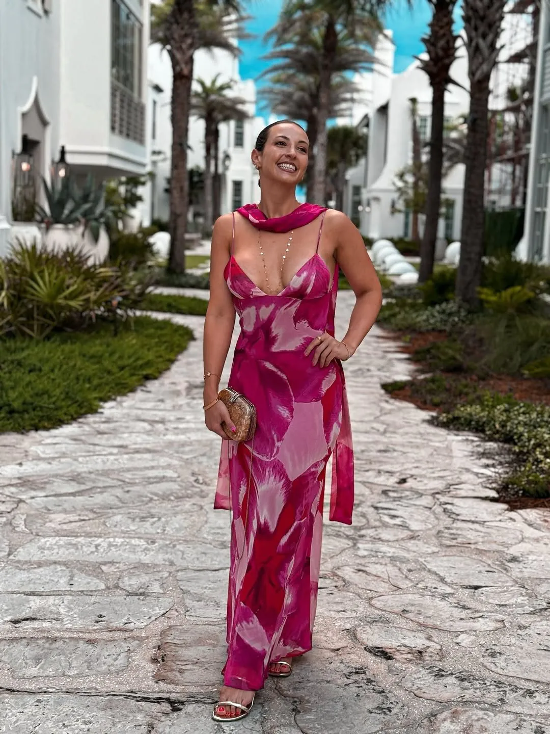 woman in a vibrant pink floral maxi dress walking along a paved resort path
