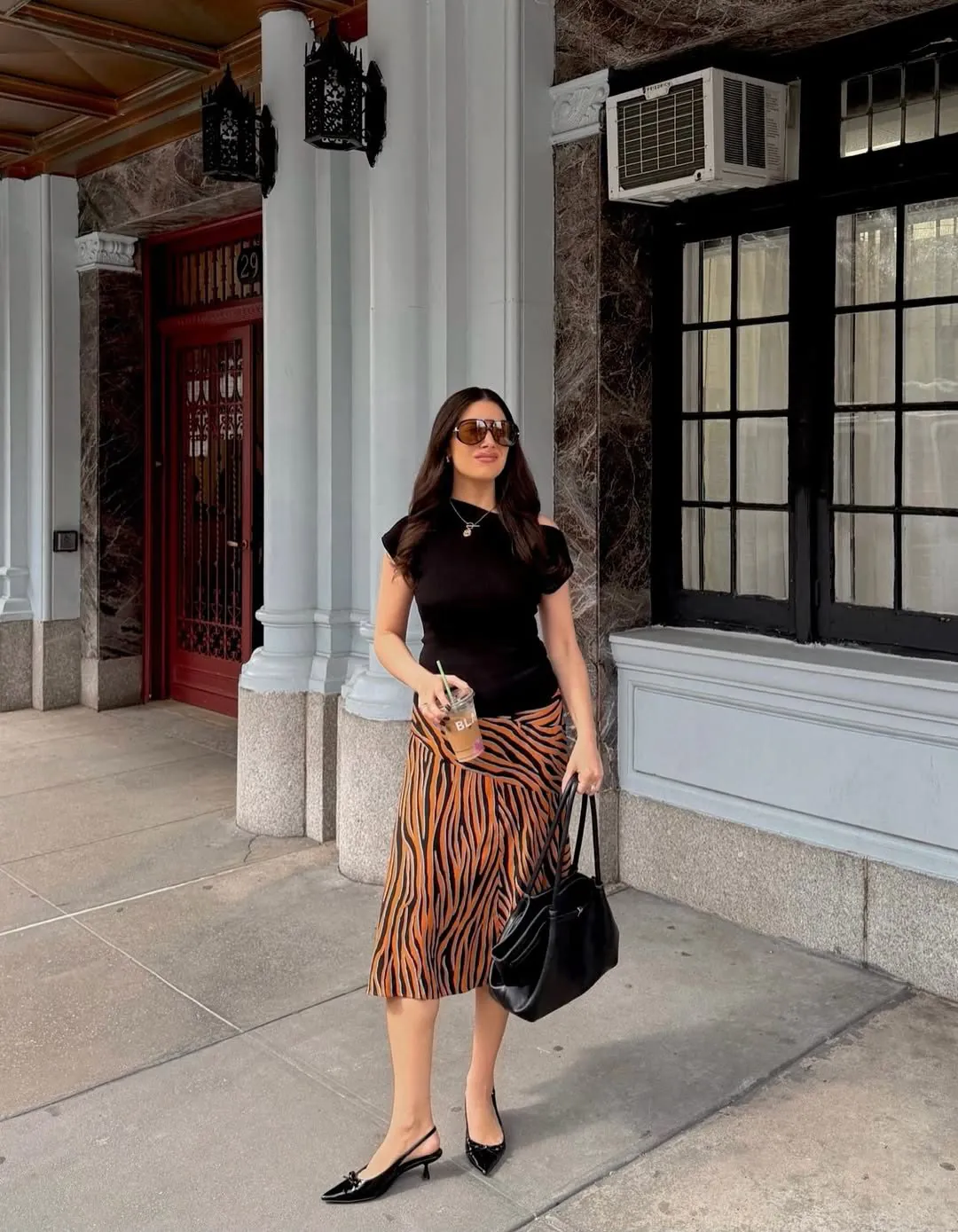 woman in a black top and orange tiger-print skirt holding an iced coffee cup