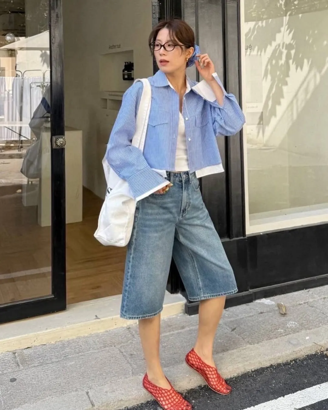 woman in a blue striped button-down shirt and denim shorts wearing red mesh flats