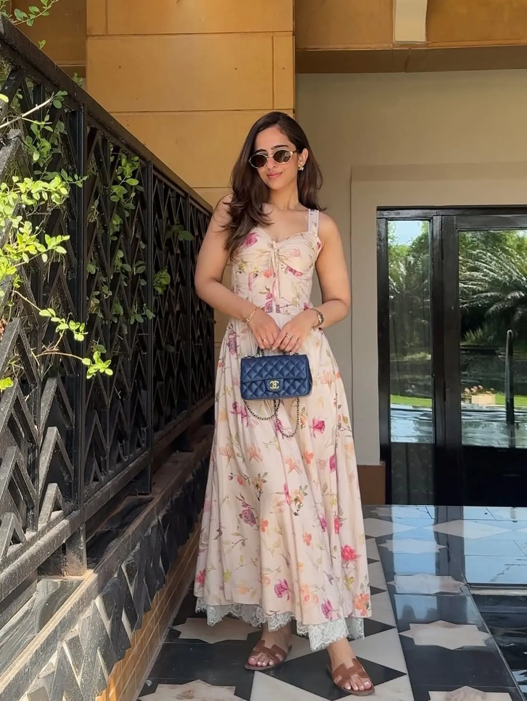woman wearing a floral maxi dress and sunglasses holding a quilted navy handbag