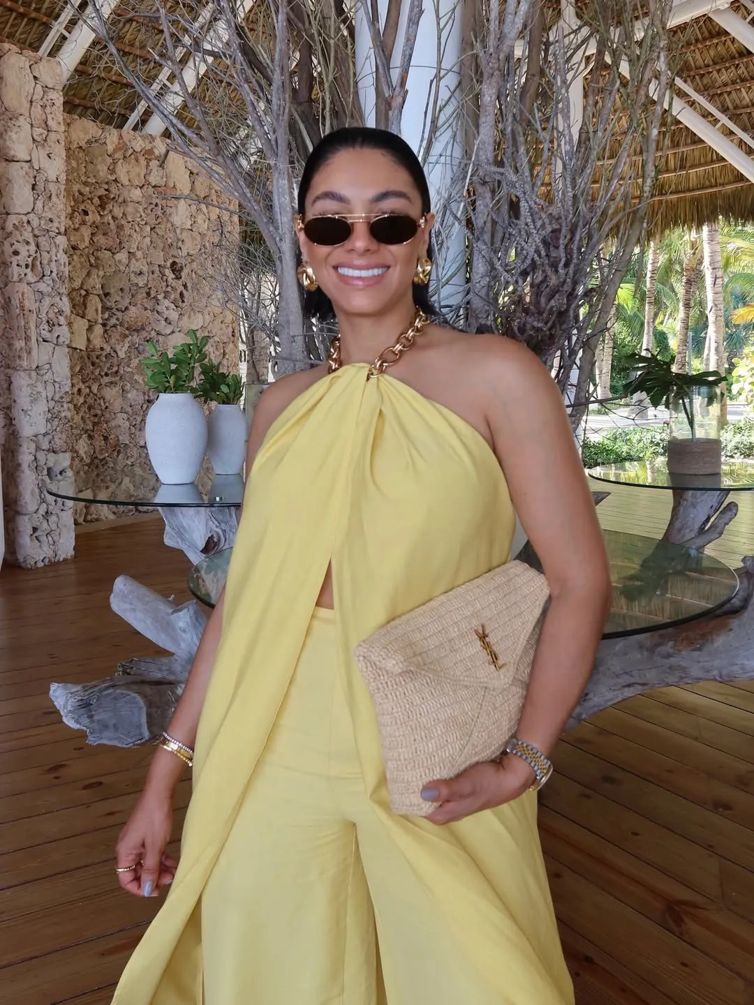 woman in a yellow halter top and matching trousers holding a woven envelope clutch