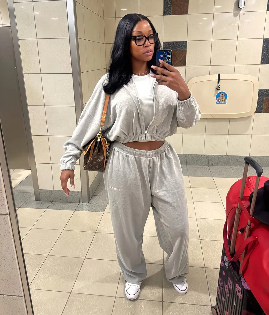 woman wearing comfortable grey tracksuit taking mirror selfie next to red suitcase