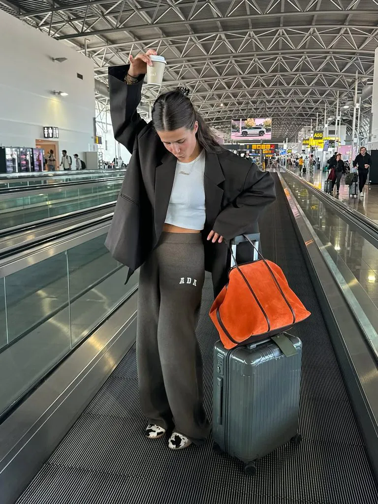 woman in dark oversized blazer and lounge pants on airport moving walkway