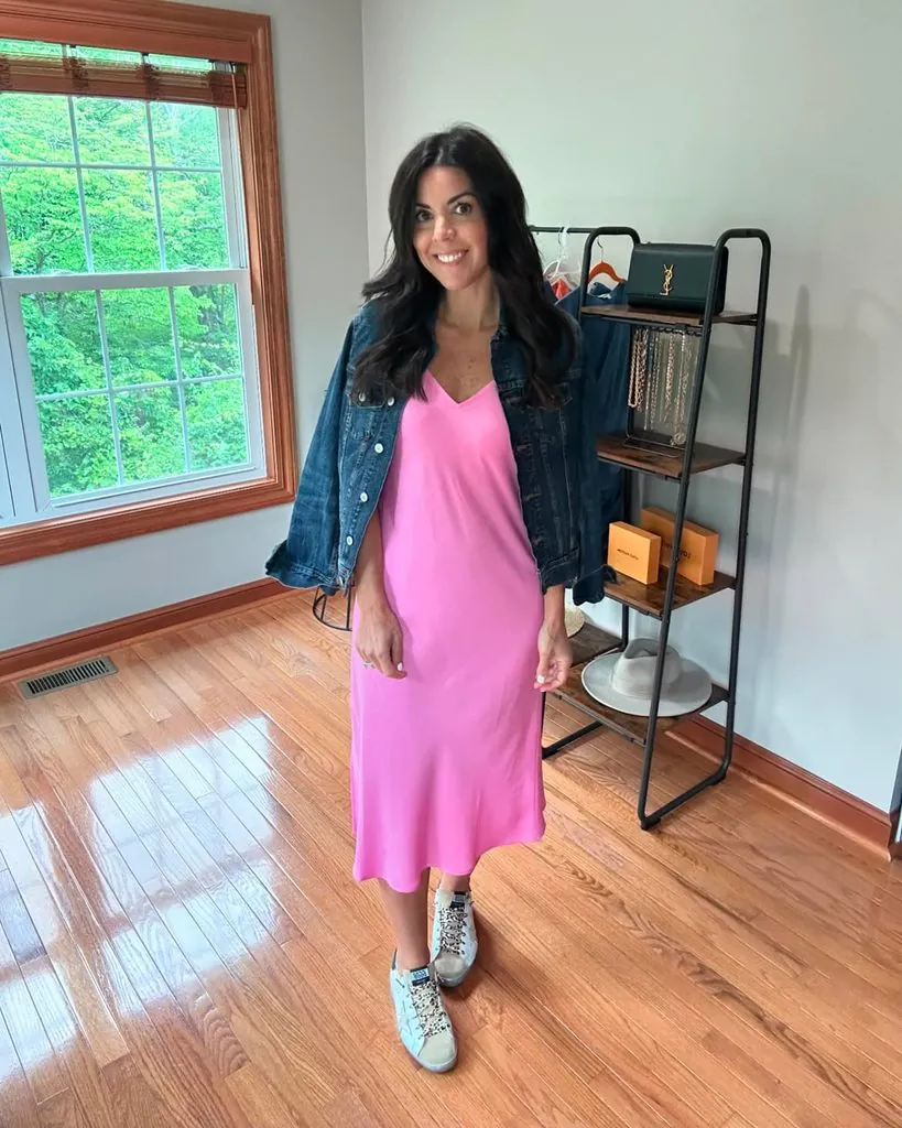 woman wearing bright pink slip dress and denim jacket with casual sneakers indoors