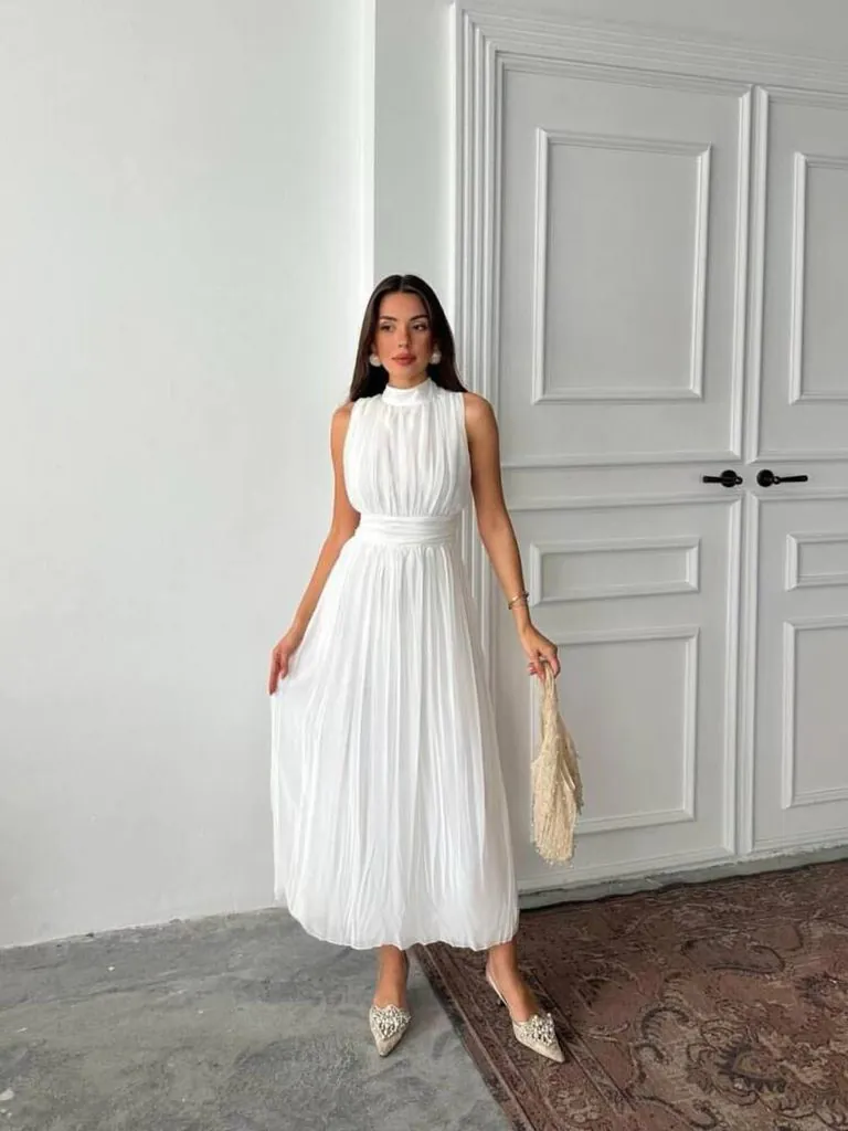 woman posing in a high-neck white pleated maxi dress all-white party outfit