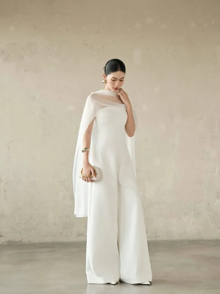 asian woman wearing a white cape jumpsuit with gold accessories all-white party outfit