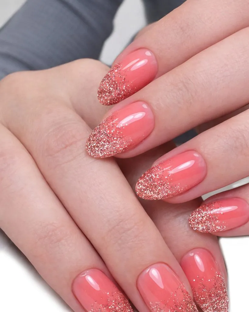 almond manicured nails with a pink base and rose gold glitter gradient tips