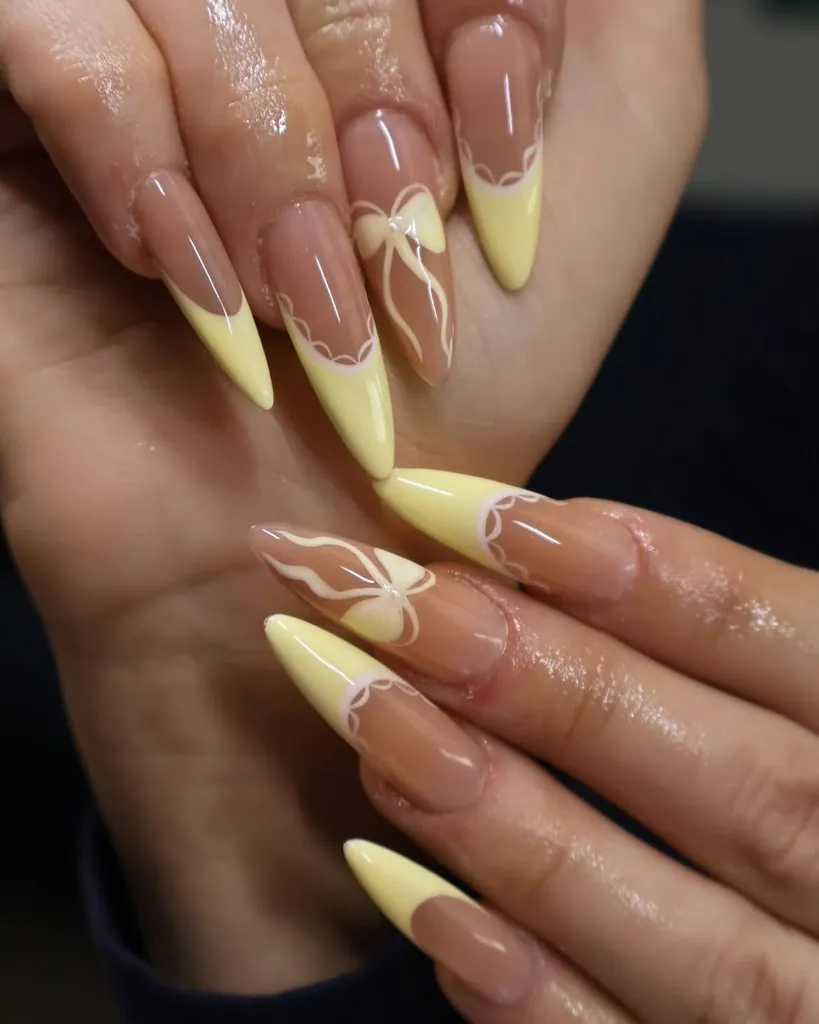 long stiletto nails with pastel yellow french tips and handpainted bow details