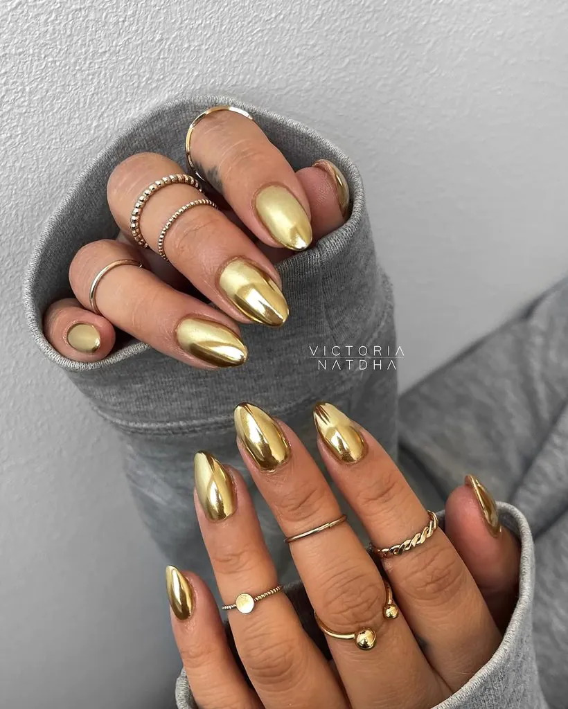 shiny metallic gold chrome almond shaped nails with gold rings on fingers