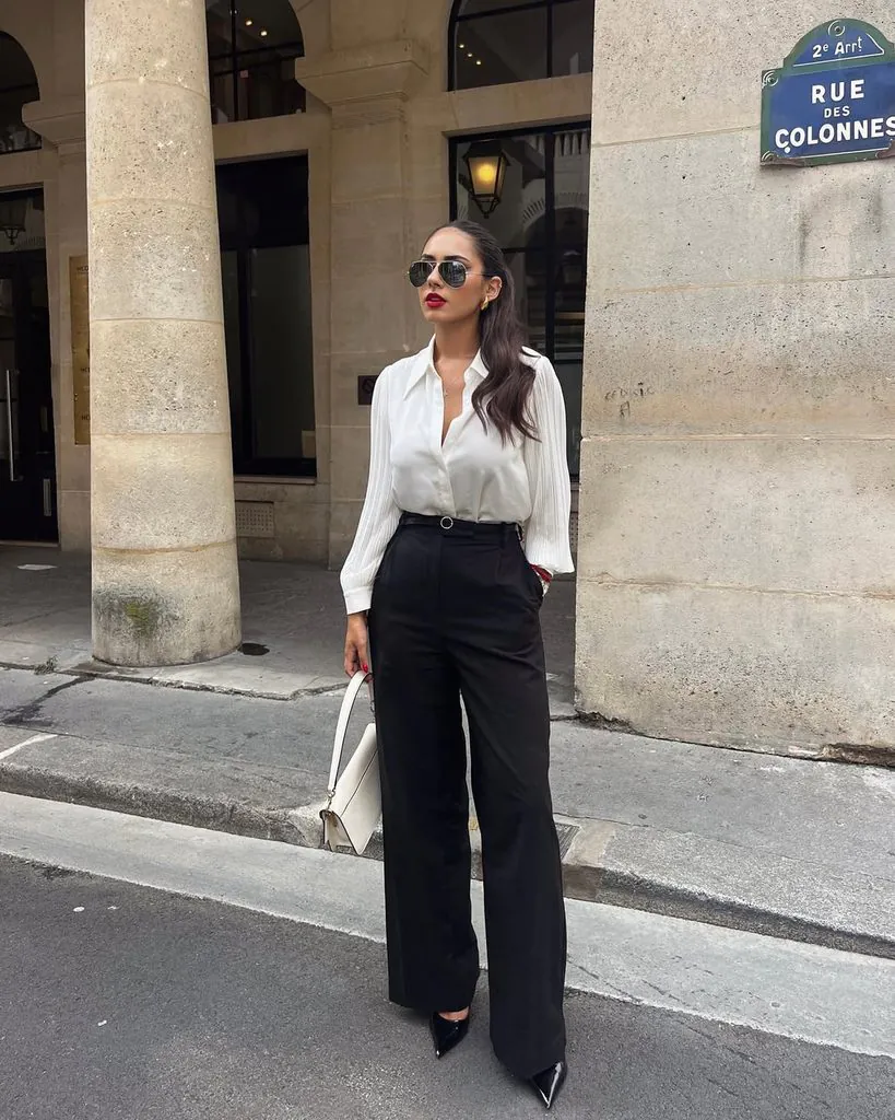 woman standing on city street wearing white button-up blouse and black trousers