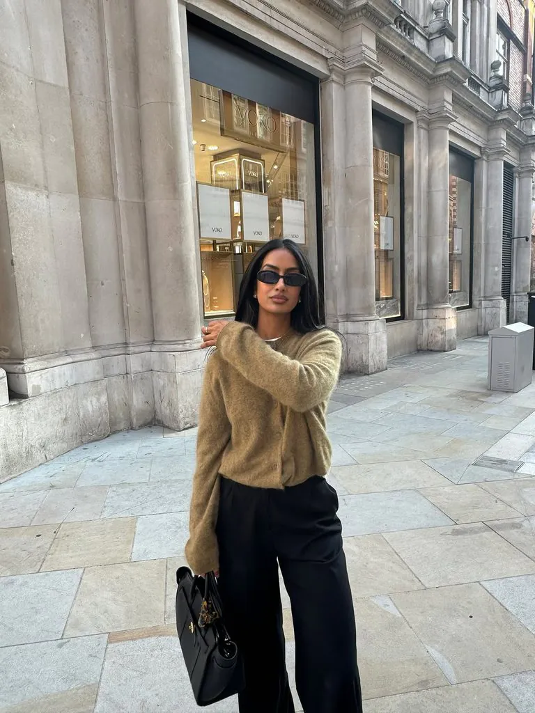 woman standing on sidewalk wearing brown cardigan sweater and black pants