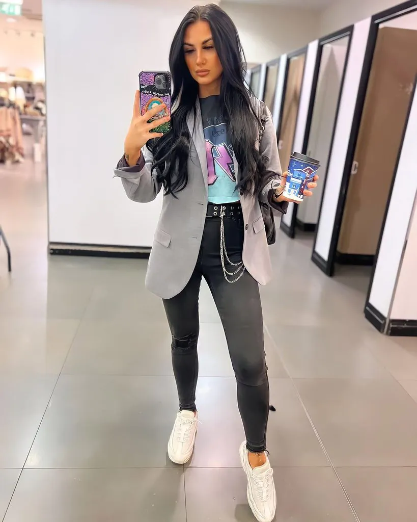 woman posing in a grey blazer, graphic tee, and black jeans with a chain