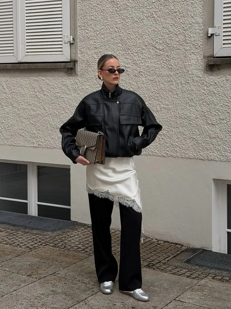 woman wearing a black leather jacket, asymmetrical satin skirt, and wide-leg black trousers