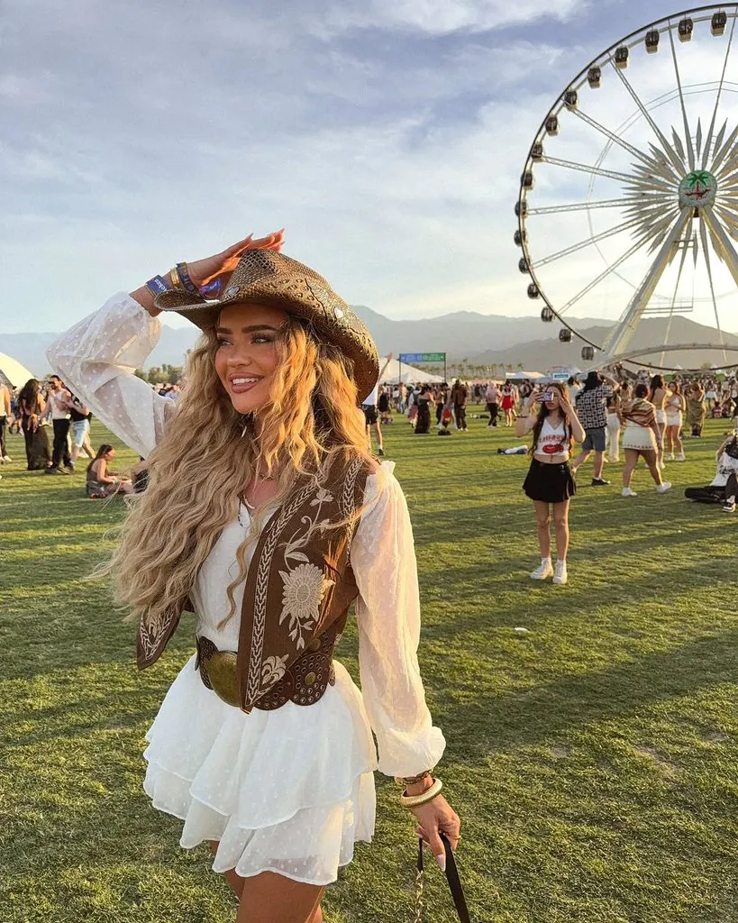 woman wearing a cowboy hat, white dress, and brown vest at an outdoor concert