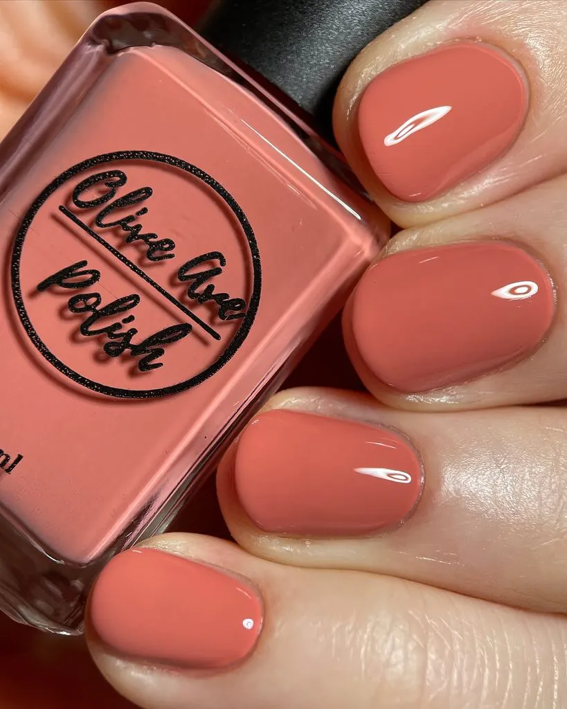 close up of coral terracotta colored nail polish bottle and matching manicure