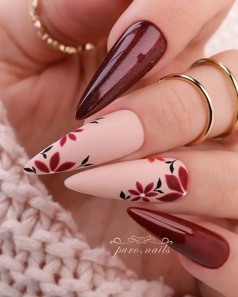 pointed fall nails featuring burgundy polish and matte nude accent nails with painted floral details