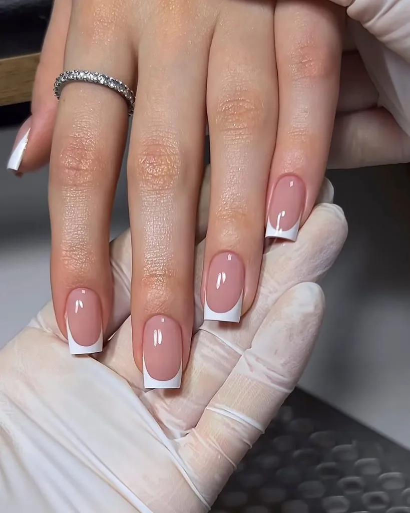 gloved hand holding square acrylic manicure with crisp white classic french tip nails