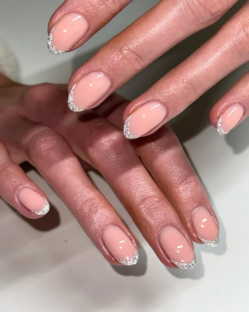 short oval manicure featuring nude pink base and reflective silver glitter french tip nails