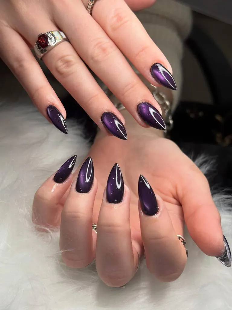 shiny dark purple cat eye stiletto nails set on a white fur background