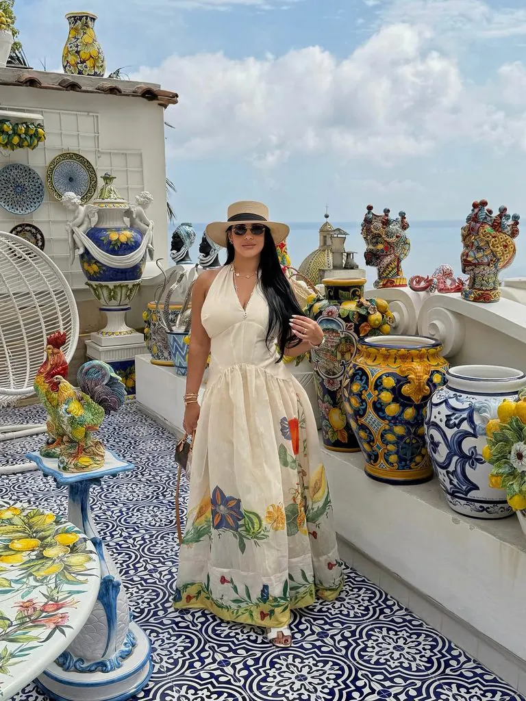 woman wearing a floral halter dress and straw hat standing on a tiled patio