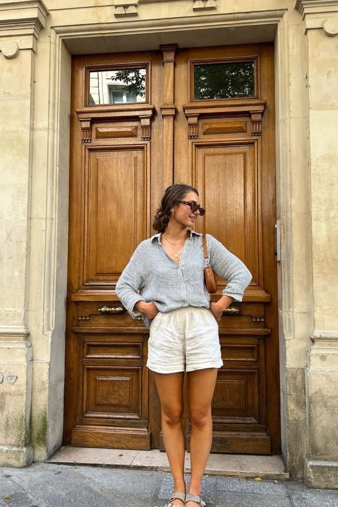woman wearing a striped button-up shirt and linen shorts in front of a wooden door