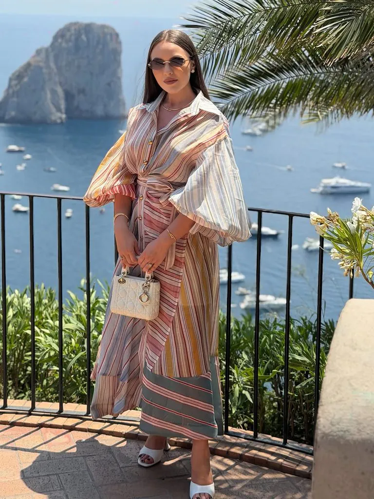 woman wearing a colorful striped midi dress with puffy sleeves overlooking coastal sea view