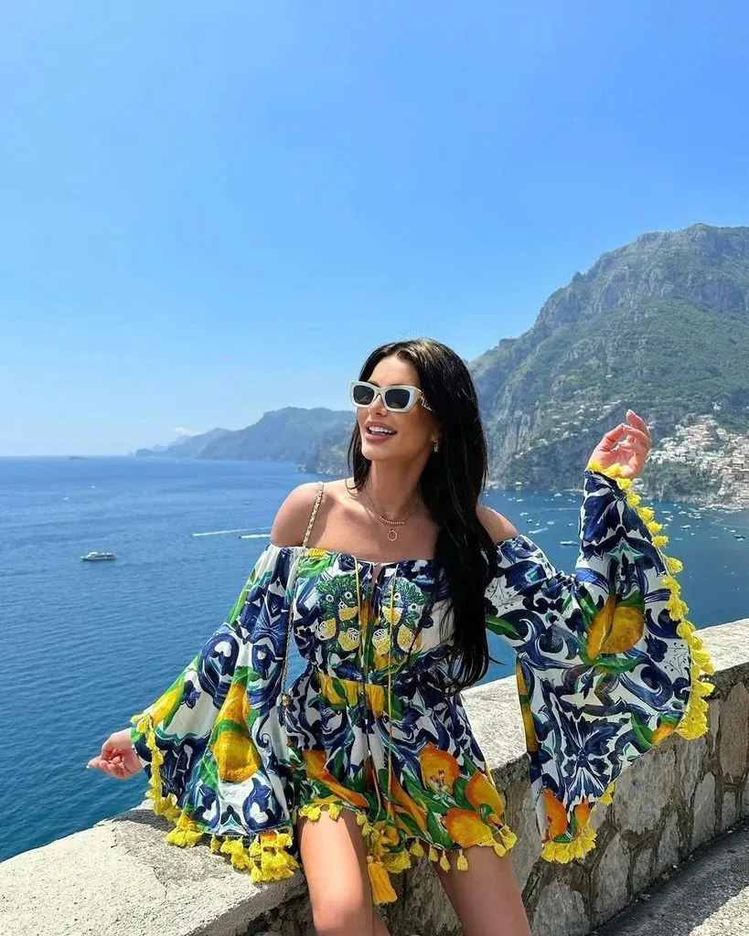 woman wearing a vibrant patterned off-the-shoulder dress for italy summer outfits by the sea