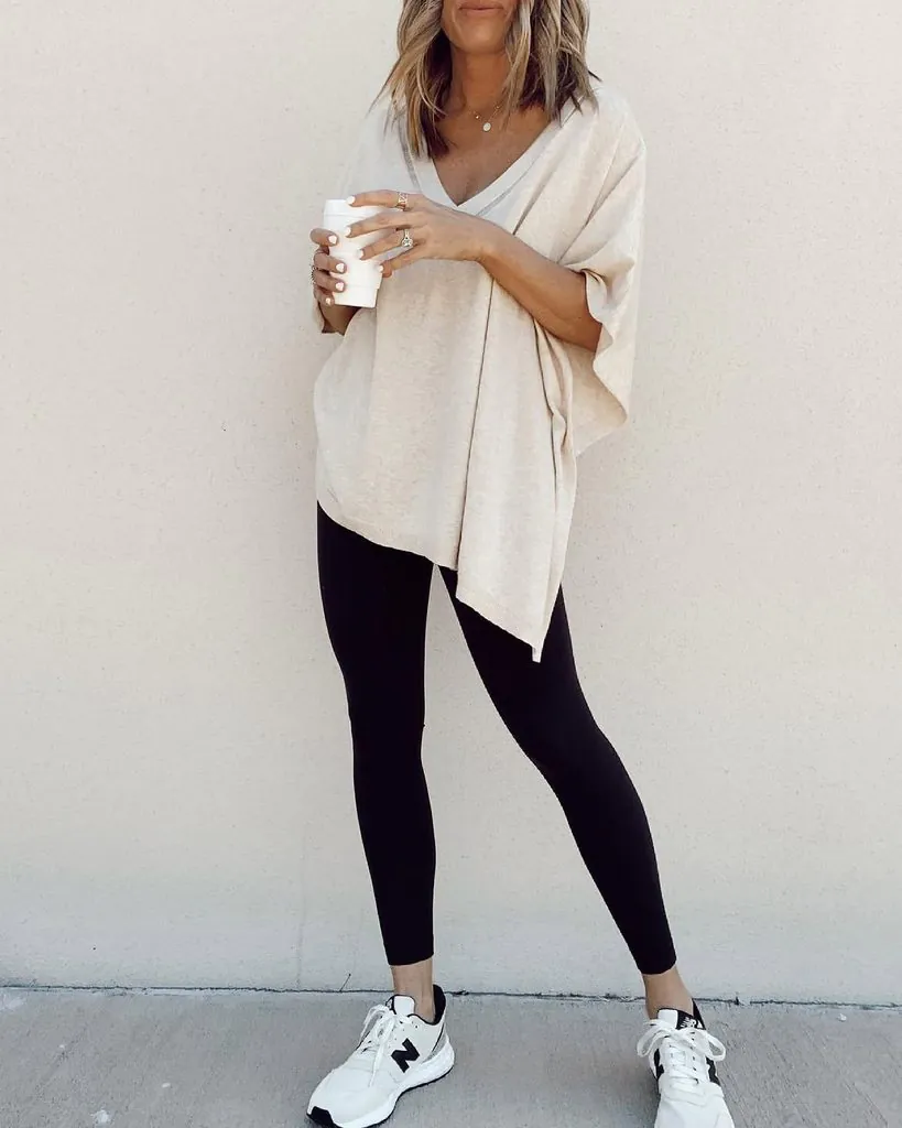 woman wearing black leggings, oversized beige v-neck top, and white sneakers