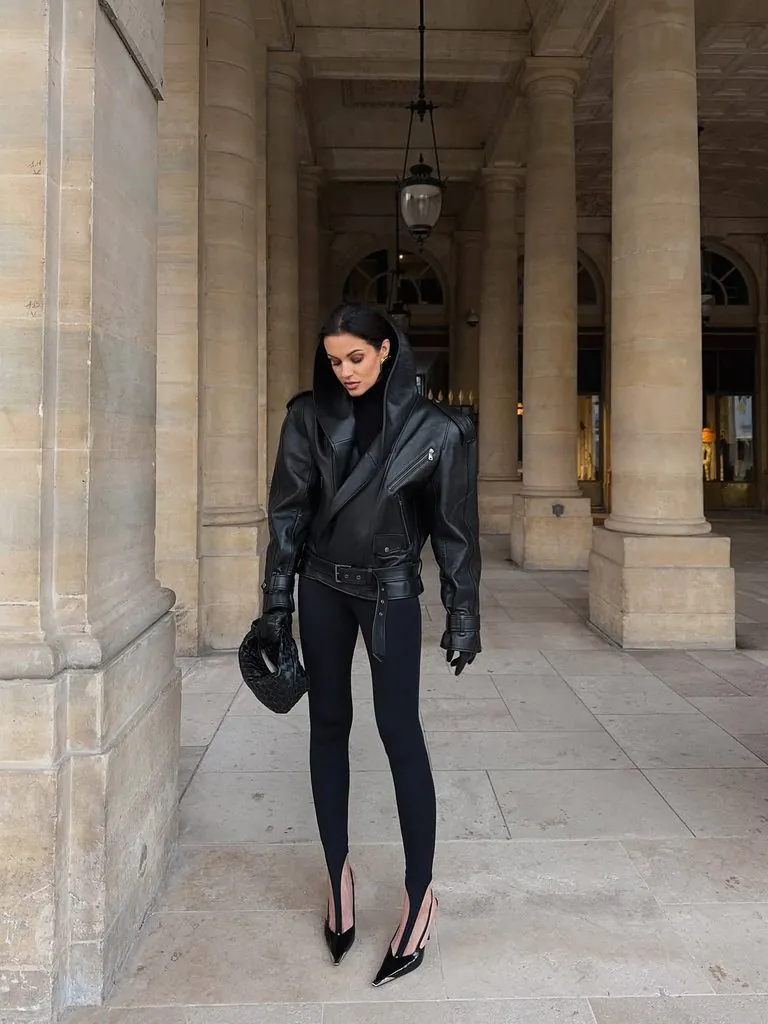 woman wearing black stirrup leggings, hooded leather jacket, and black high heels outdoors