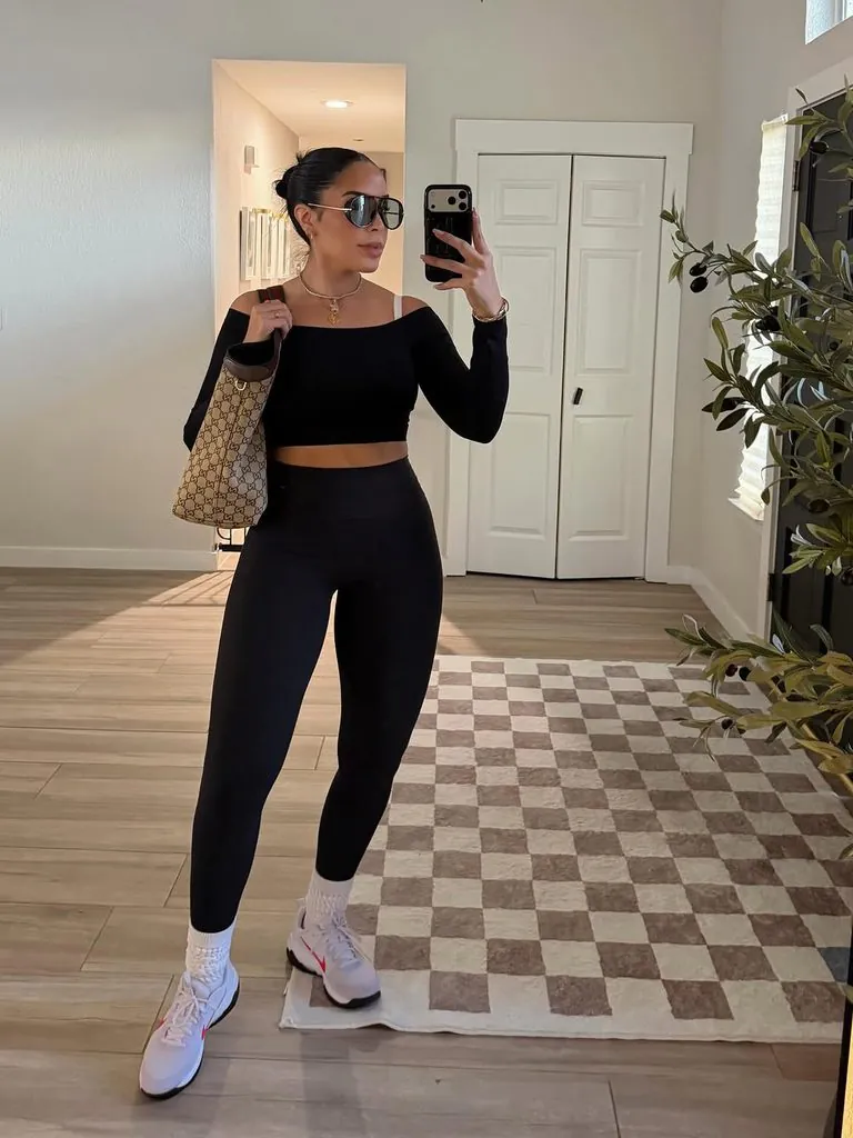 woman taking mirror selfie in black leggings, off-shoulder top, and white sneakers