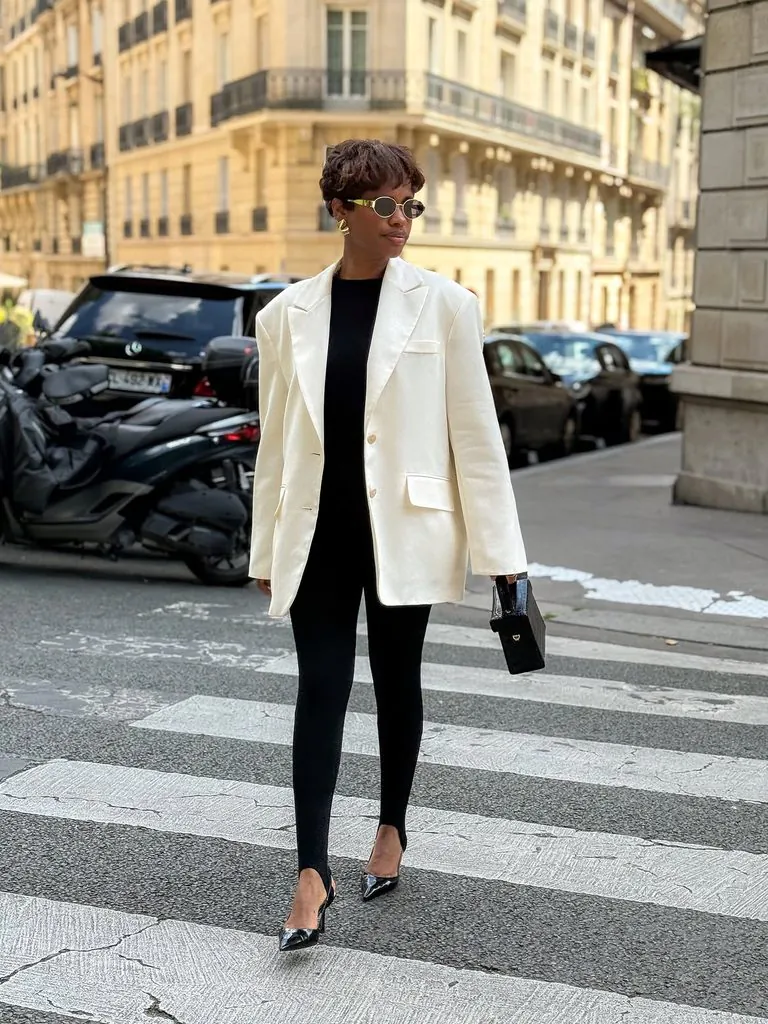 woman crossing street in black stirrup leggings, oversized white blazer, and heels
