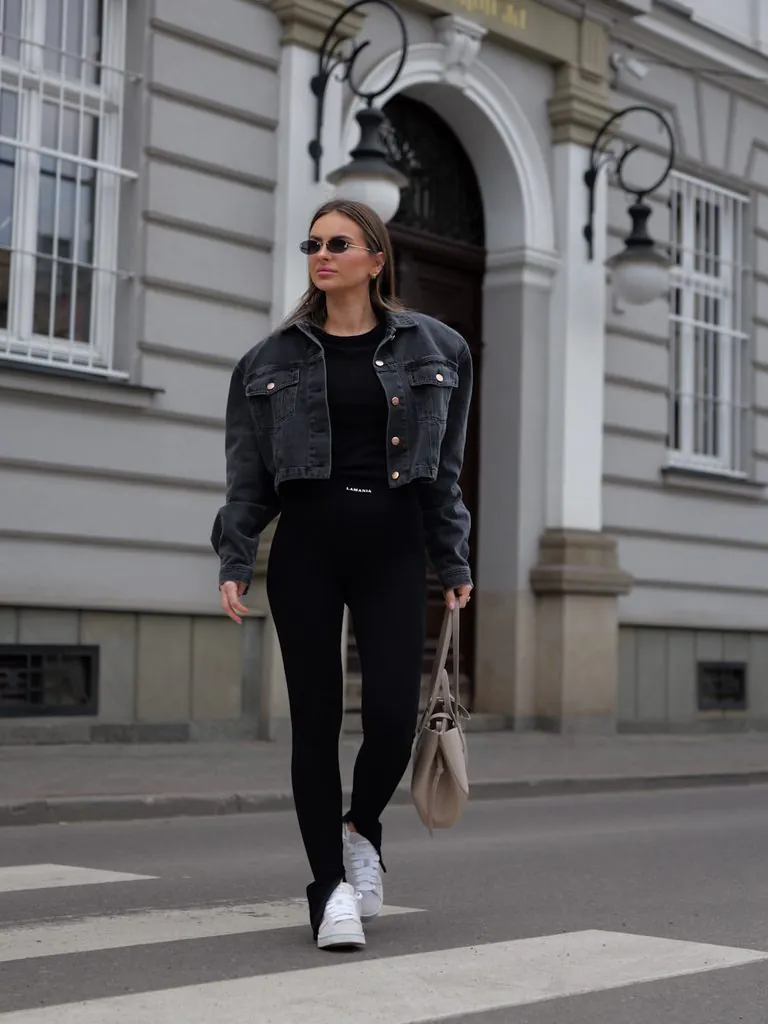 woman walking in black leggings, cropped grey denim jacket, and white sneakers