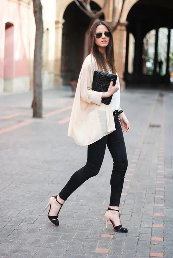 woman walking in black leggings, beige cardigan, and high heels holding a clutch