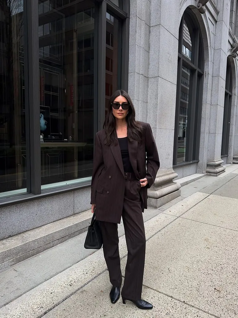 woman wearing a dark brown pinstripe suit with black top, handbag, sunglasses outdoors