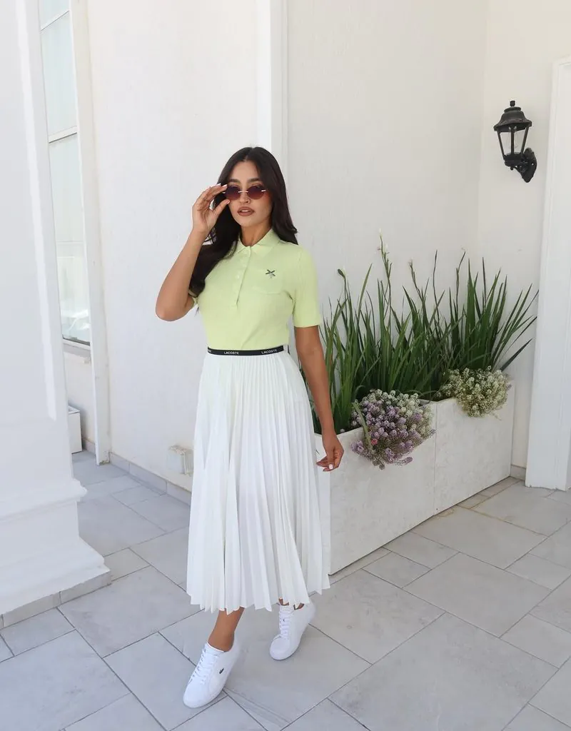 woman wearing lime green polo shirt, white pleated skirt, sunglasses, and white sneakers