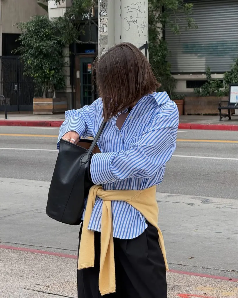 woman wearing blue striped shirt, black pants, and yellow sweater tied around waist