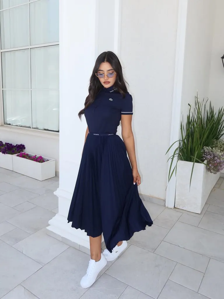woman wearing navy polo shirt, pleated skirt, sunglasses, and white sneakers