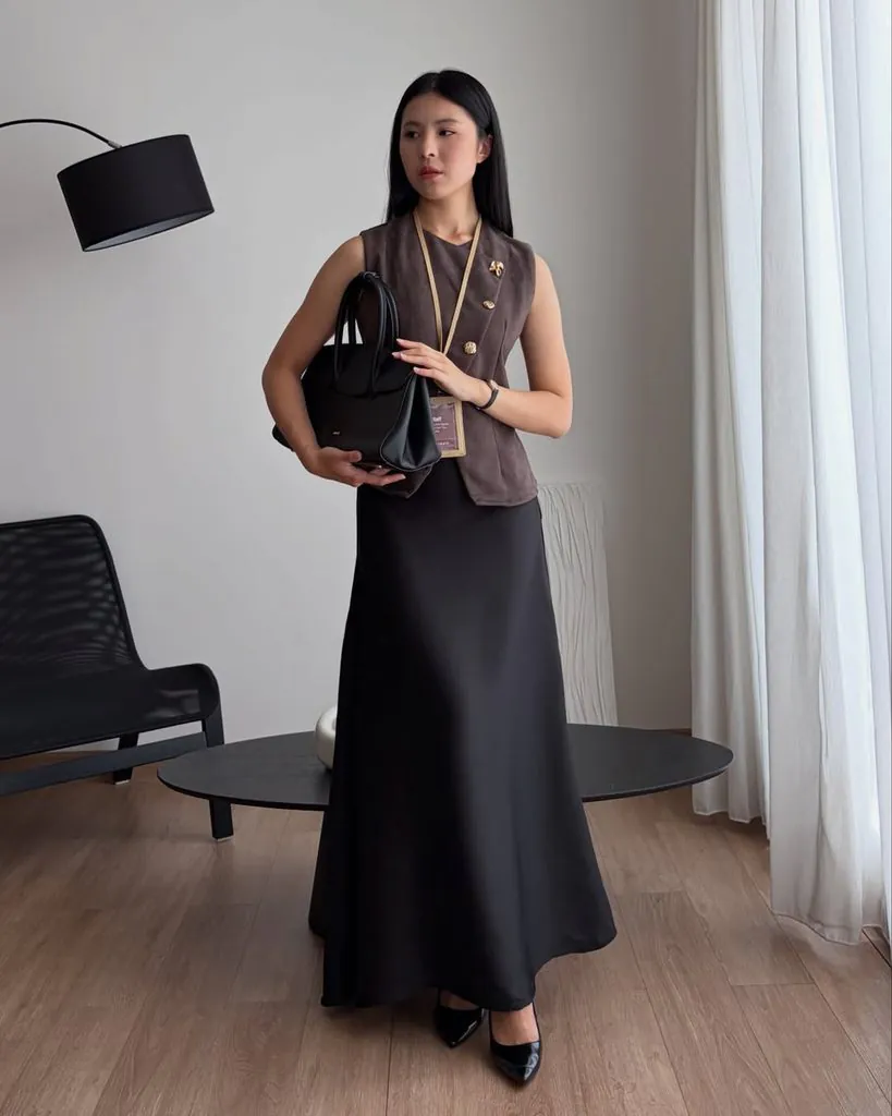 woman wearing a brown sleeveless vest and a black maxi skirt while holding a purse