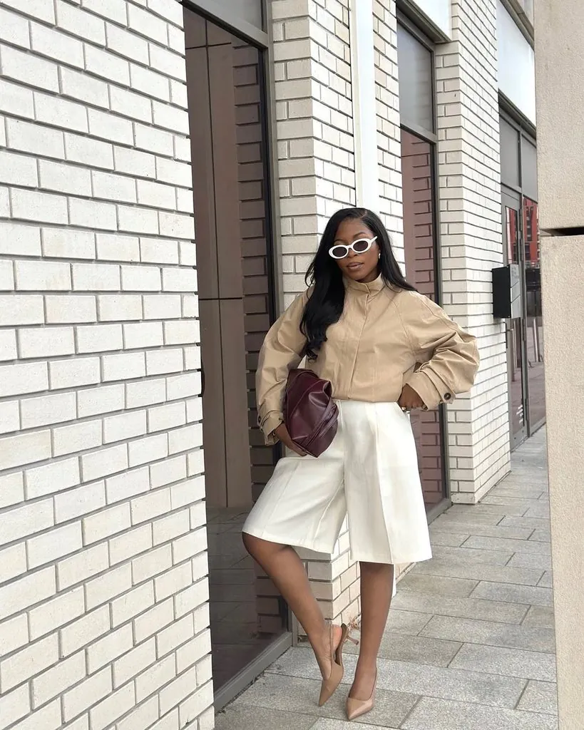 woman wearing white sunglasses, a beige jacket, and white wide-leg shorts outside turn