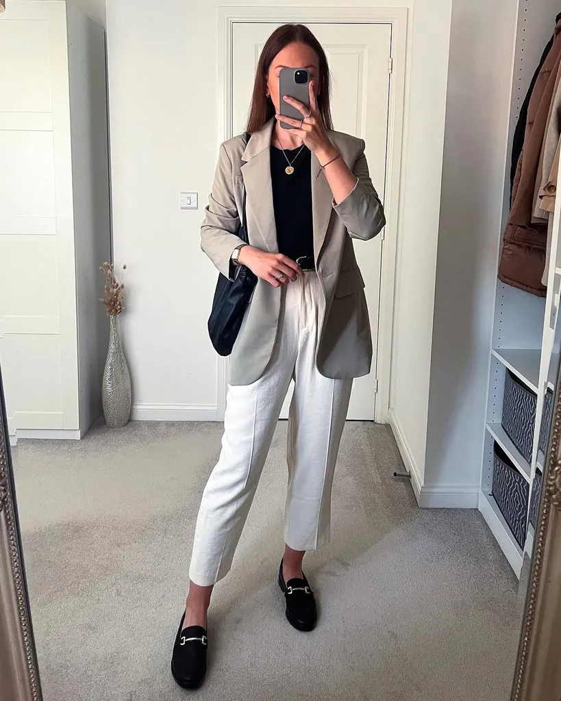 woman wearing a grey blazer, black t-shirt, white trousers, and black loafers