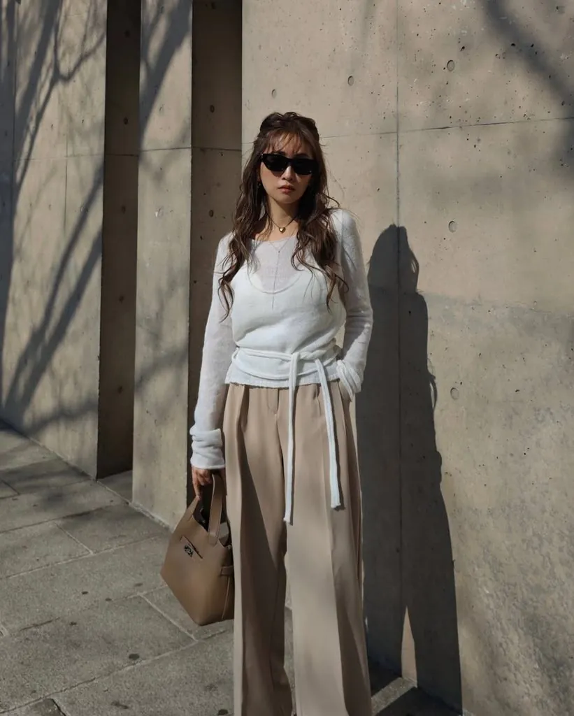 woman in sunglasses wearing a white tie-waist sweater and beige wide-leg trousers outdoors