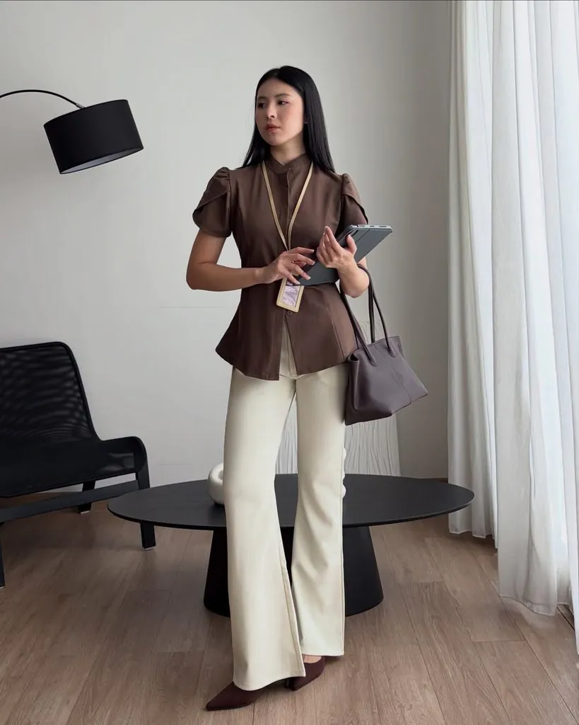 woman wearing a brown short-sleeve blouse and cream wide-leg trousers holding a tablet