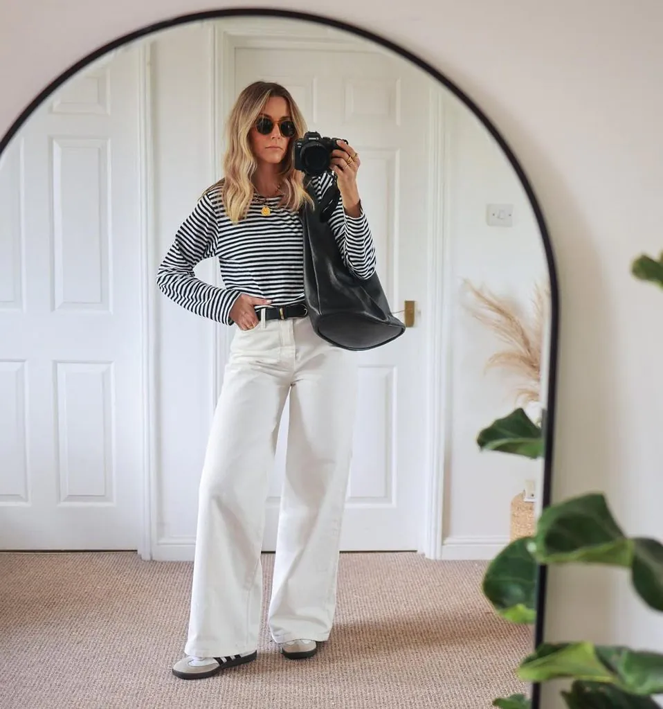 woman taking mirror selfie wearing a striped long sleeve shirt and white jeans