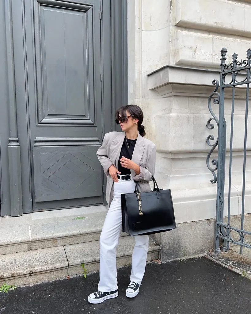 woman standing outside wearing a grey blazer, black t-shirt, and white jeans