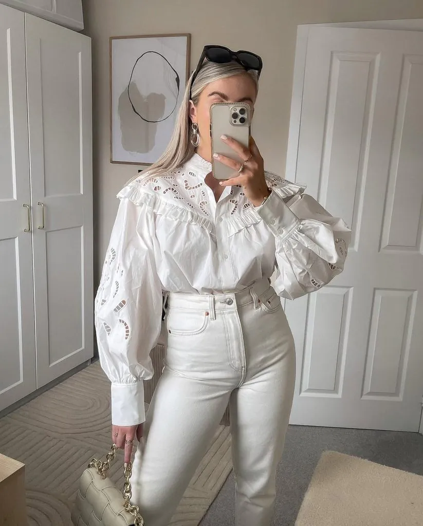woman taking mirror selfie wearing structured white ruffle eyelet blouse and white jeans