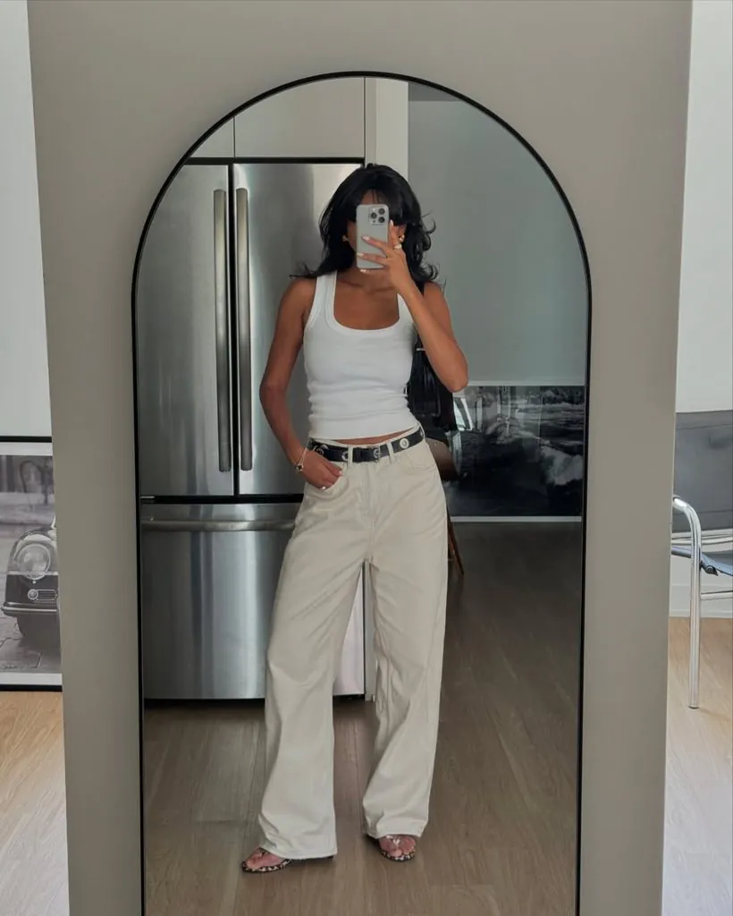 woman taking mirror selfie wearing a white tank top and wide-leg white jeans