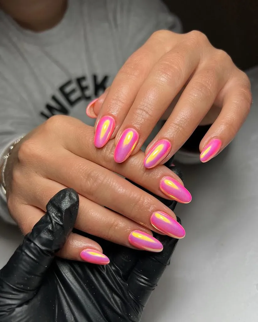 vibrant pink chrome almond nails with yellow iridescent shimmer held by gloved hand